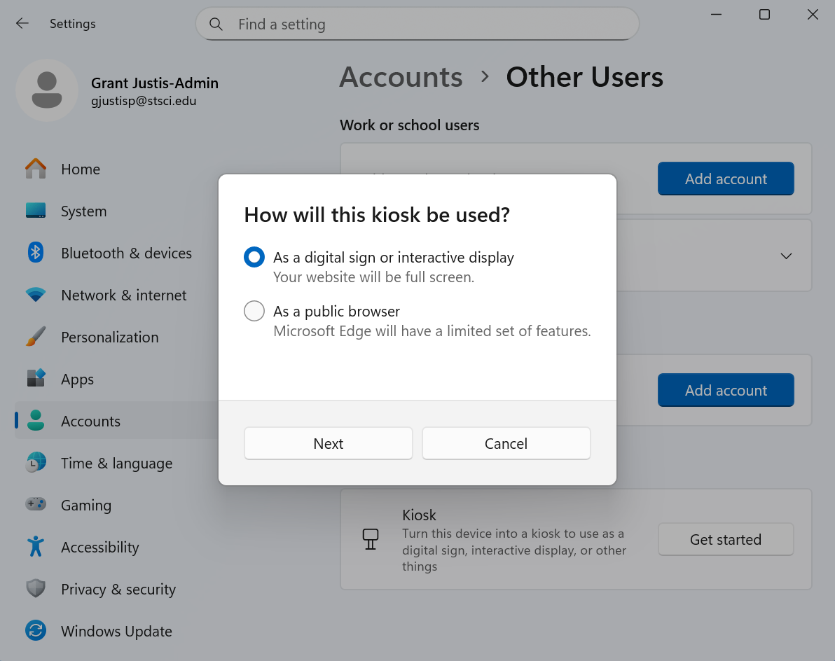 Dialog box titled “How will this kiosk be used?” within the Windows Settings under “Accounts > Other Users.” The user is prompted to choose between two options: “As a digital sign or interactive display” (selected), and “As a public browser.” Below are “Next” and “Cancel” buttons.